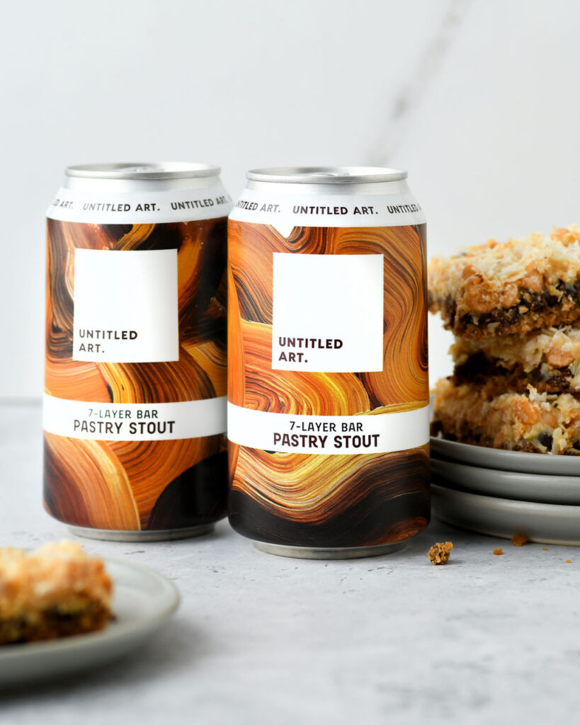 Two cans of '7-layer bar pastry stout' beside a stack of dessert bars.