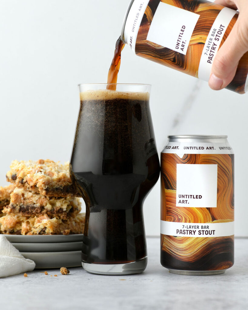 Pouring a dark stout beer into a glass with a dessert bar on the side.