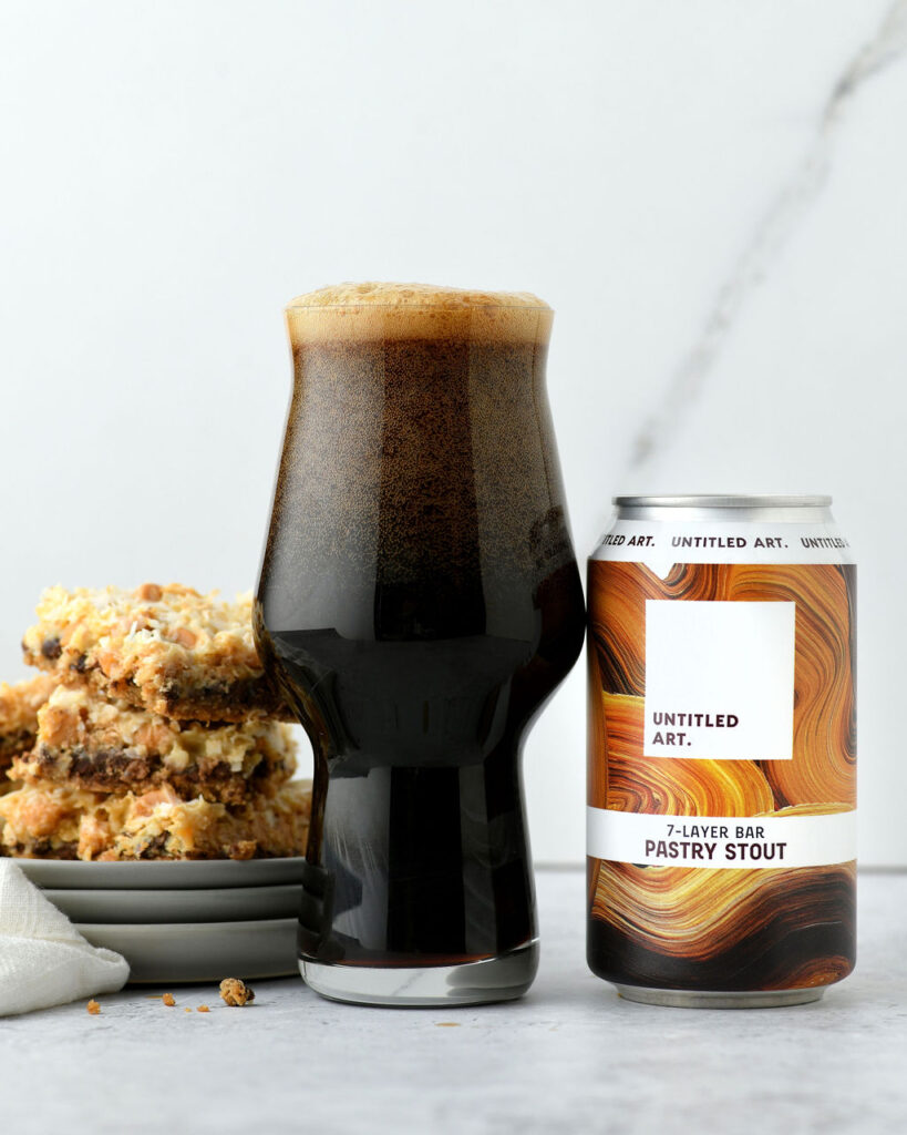 A glass of dark stout beer next to its can and a stack of dessert bars.